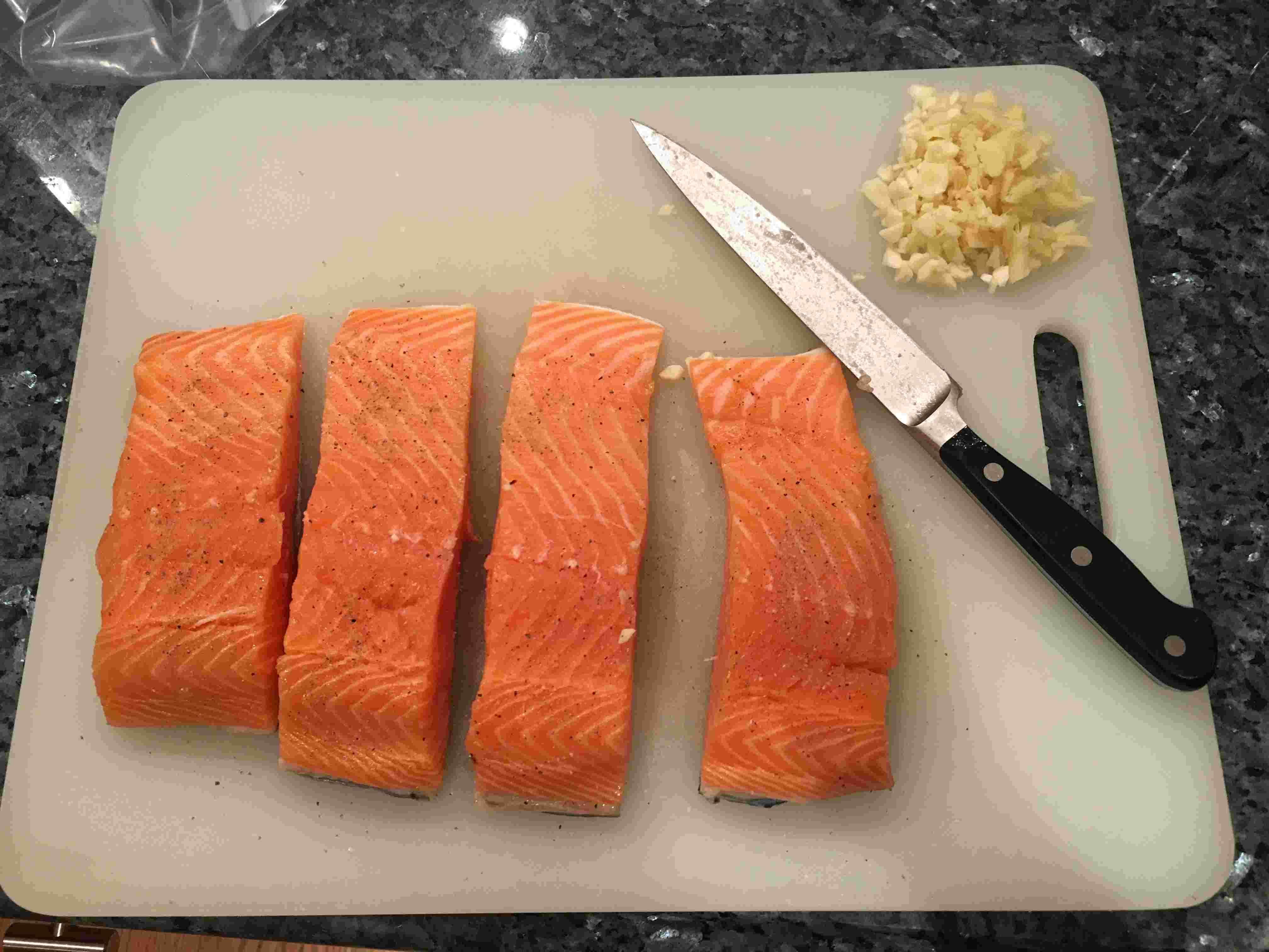 Salmon is seasoned with salt and pepper. Garlic and ginger are ready for the kale.